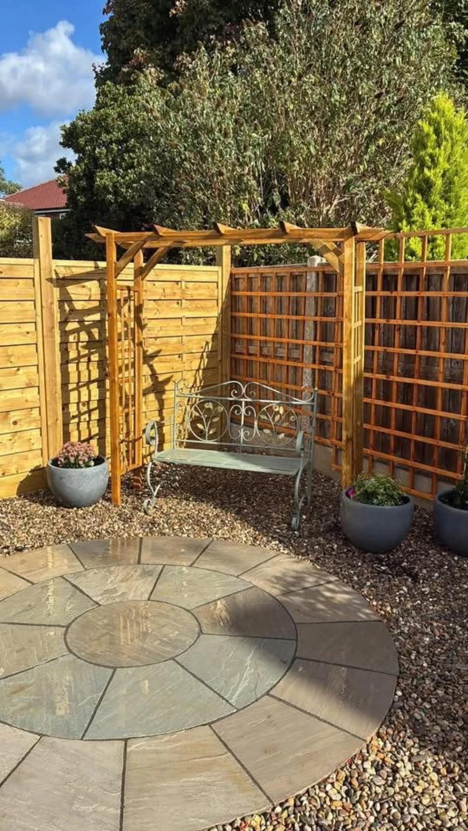 Timber arbour with bench and trellis over a circular paved area