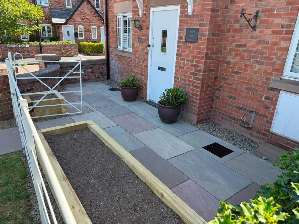 Sandstone paved front garden with sleeper raised bed and potted plants