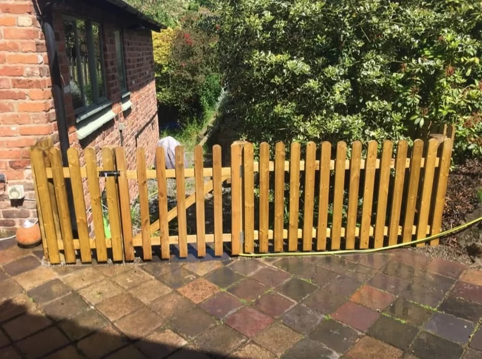 Timber picket fence and gate beside a brick house