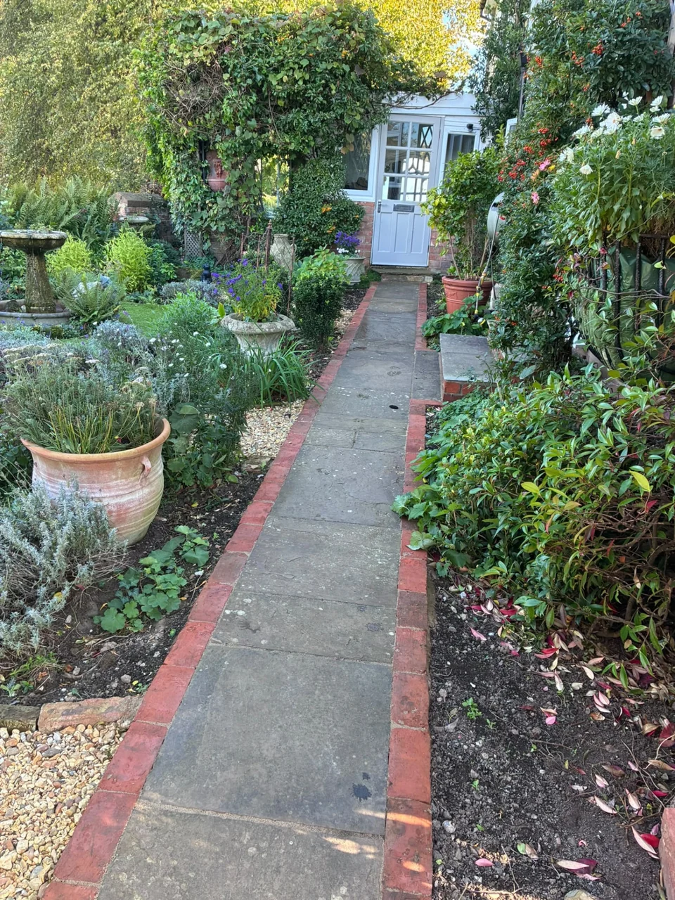 Narrow sandstone garden path with brick edging through planted borders