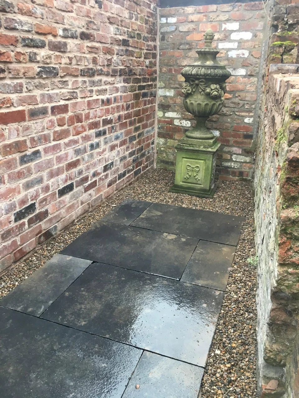 Slate paving in a brick-walled courtyard with stone urn