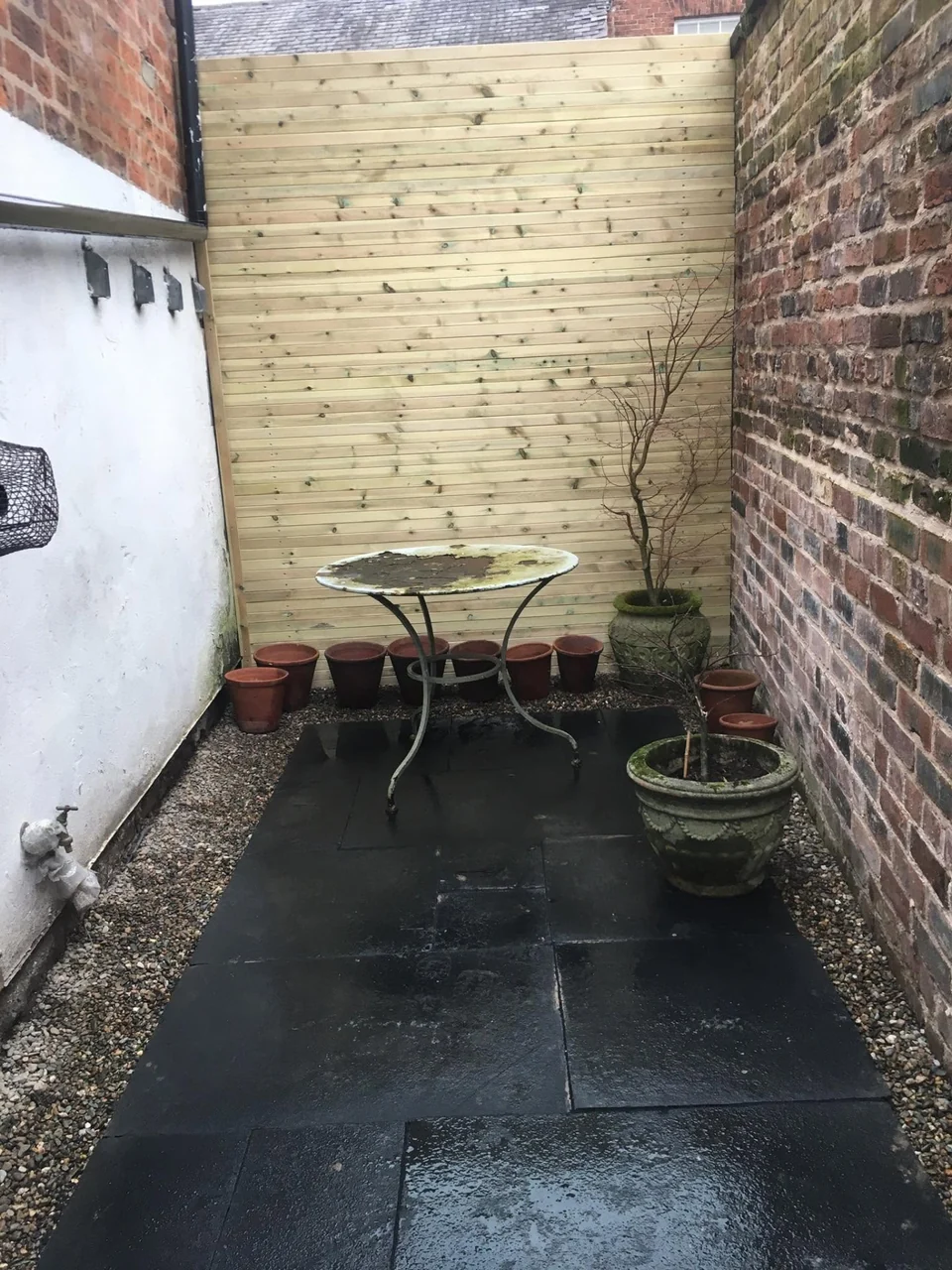 Dark slate paved courtyard with new fence and potted plants