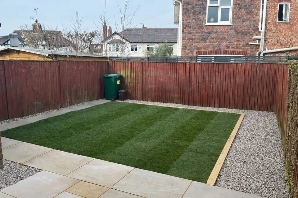 Landscaped garden with striped lawn, sandstone paving, gravel edging and stained fence