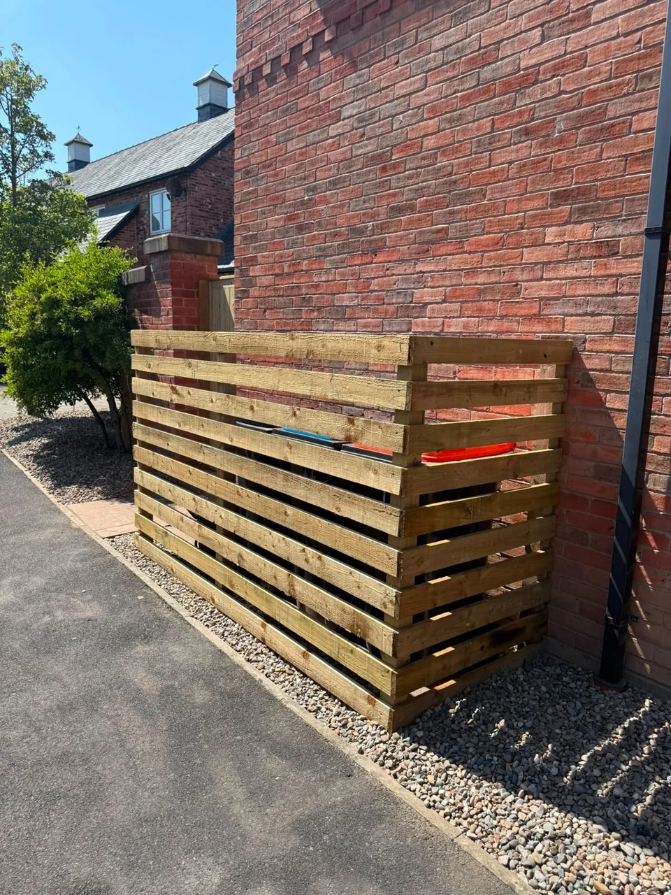 Horizontal slatted timber bin store screen beside a brick wall
