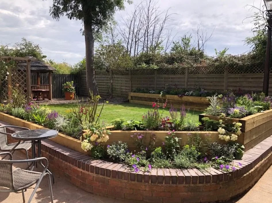 Flowering garden with curved brick raised border, timber planting beds, lawn and gazebo