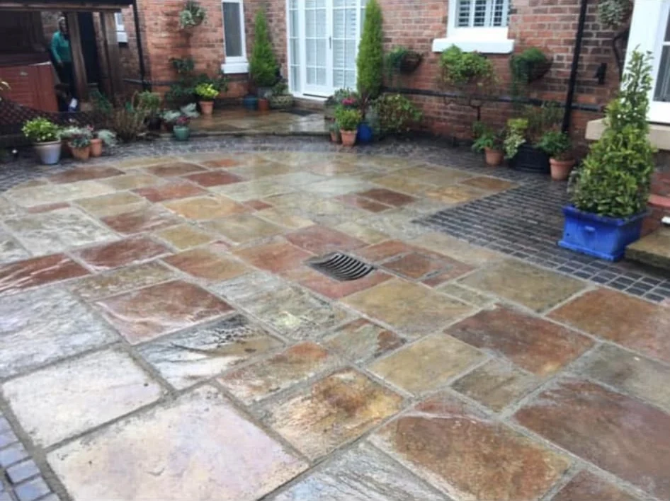 Sandstone courtyard patio outside a brick house with potted plants and dark paving edging