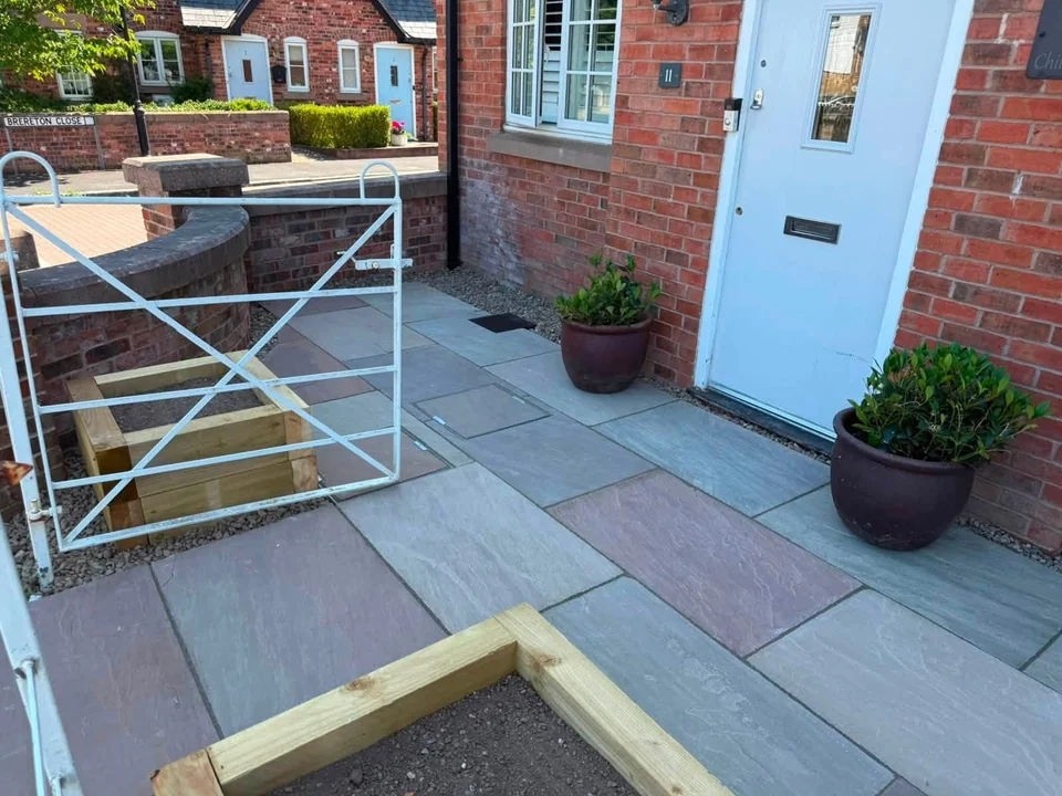Sandstone front patio with sleeper planters and white metal gate