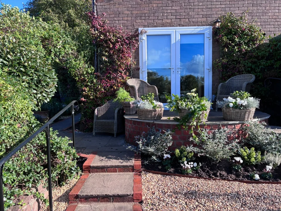 Garden patio with wicker chairs, planted baskets, curved brick retaining wall and stone steps