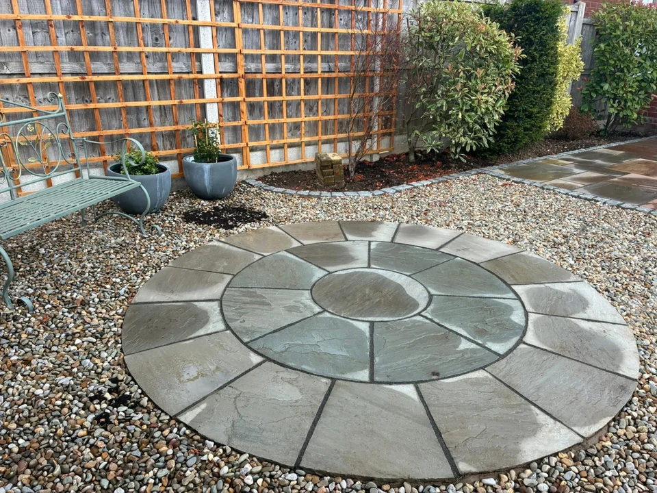 Circular sandstone paving feature set in gravel beside trellis fencing