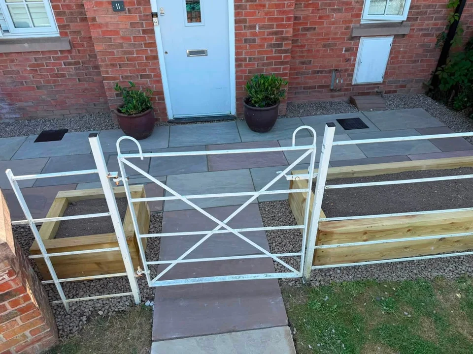 Sandstone paved path through a white gate between sleeper beds