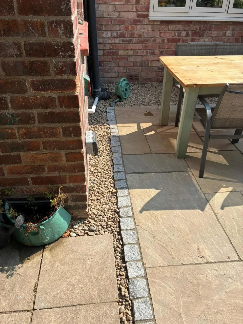 Sandstone patio with granite sett edging beside a brick house